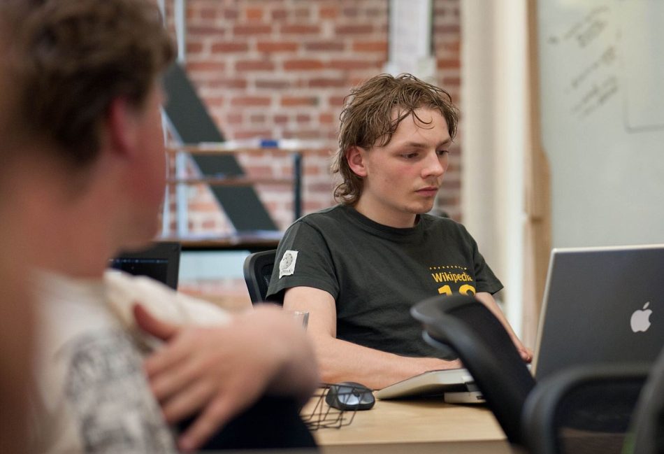 A programmer reviewing lines of code on a large monitor in a dim office.