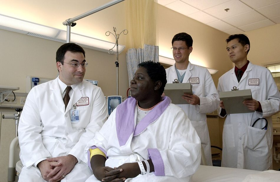 Doctors in white coats talking with a woman patient in a hospital room